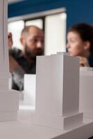 Closeup of white foam architectural scale model of residential building complex in front of architects team working together. Detail of urban development project on design table. photo