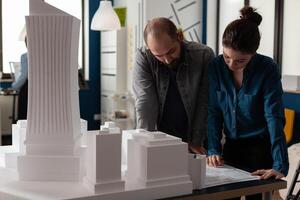 Team of two architects colleagues collaborating looking down at blueprints of urban planning project. Architectural engineers doing teamwork reading construction plans. photo