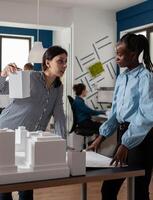 Architect presenting foam scale building model to engineer coworker standing next to residential project maquette in modern architectural office. Team of architects doing creative thinking. photo