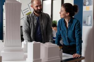Architects doing teamwork looking at each other discussing blueprints in modern architecture office. Team of two architects colleagues working together at urban planning project. photo