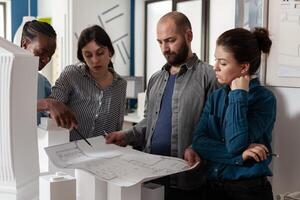 Team of architects analyzing blueprints for building project standing in front of table with real estate maquette. Professional engineers reading construction plans for urban development. photo