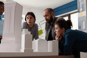 Team of professional architects looking at skyscraper maquette in architectural office. Engineer partners working on group project at desk with real estate construction model. photo