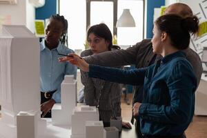 Team of professional architects brainstorming ideeas pointing at real estate construction model in architectural office. Mixed group of engineers working on residential project at desk. photo