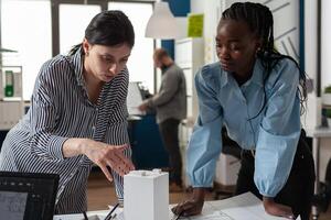 Architect colleagues discussing design of white foam building model in modern architectural office. Team of two professional architects working on blueprints on desk. photo