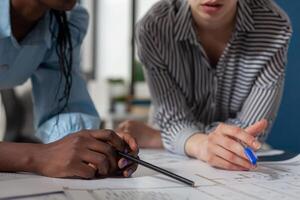 Closeup view of mixed race architects holding pencil and pen over blueprints at architectural desk. Detail of engineer hands over technical drawing construction plans of residential project. photo