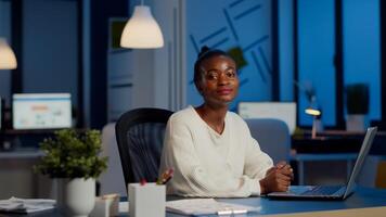 Tired black woman manager looking at camera sighing after typing on laptop, working late at night in start-up financial business office. Focused employee doing overtime respecting deadline of project photo