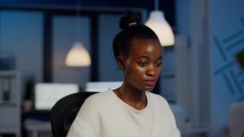 African bookkeeper working overtime calculating profit, taking notes, analysing financial documents sitting at desk in start-up financial company. Overworked woman doing overtime respecting deadline. photo