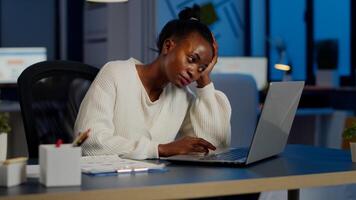 Exhausted african freelancer resting head on hand in front of laptop working overtime in start up company office. Stressed employee using modern technology doing overtime for deadline of project photo