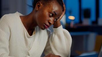 Tired black woman almost napping on chair working on laptop in start up company office late at night. Busy employee using modern technology doing overtime to finish project, respecting deadline photo