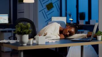 Exhausted overload african business woman falling asleep on desk with open laptop monitor while working in start up company. Overworked employee using doing overtime respecting deadline, sleeping photo