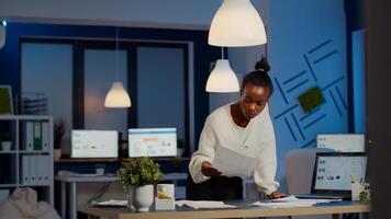Black bookkeeper working on financial reports checking statistics graphs, looking at laptop, pointing to numbers standing at desk late at night in start-up office doing overtime to respect deadline photo