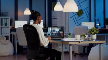 Black woman freelancer discussing with paralyzed client on call at midnight from business office using headphone. Businesswoman using virtual conference talking on webcam during online meeting photo