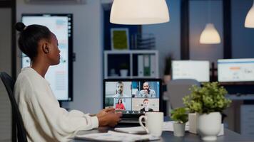 African businesswoman talking during conference with team in midnight using laptop in start up business office. Diverse workers talking during corporate meeting using technology network wireless photo