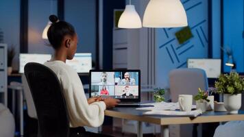 African employee working overtime from business office late at night discussing with partners online using webcam. Diverse team talking during corporate meeting using technology network wireless photo