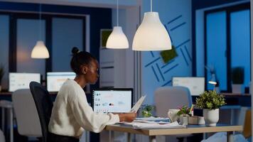African businesswoman reading business reports from laptop in start up office late night typing new project. Focused employee doing overtime for job respecting deadline of project writing, searching photo