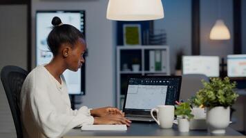 African architect analysing digital plans from laptop working in start-up business office overtime. Designer using cad software to design a 3D concept of buildings creating late at night photo