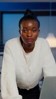 Focused tired business woman looking at camera after reading tasks on laptop standing near desk in start-up company late at night. Employee doing overtime for job respecting deadline photo