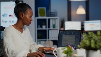 Black woman engineer designer looking at laptop analysing project using new software to design 3D concept of container working overtime in start-up company for prototype. Overworked worker studying photo