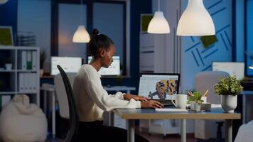 African engineer working late at night on a 3D model of industrial gears at laptop doing overtime in start up office. Freelancer studying prototype idea on pc showing cad software on device display photo
