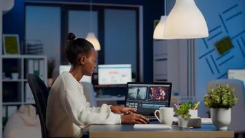 Black editor working overtime at new project editing audio film montage sitting in start-up business office. Woman content creator using professional laptop, modern technology, network wireless photo