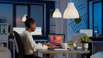 Dark skin gamer developer working at game in midnight from business office using professional laptop. African player testing online games on pc with modern technology network wireless. photo