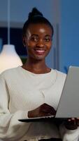 Happy african freelancer looking at camera smiling holding laptop standing near desk in start-up company late at night. Focused employee doing overtime for job respecting deadline of financial project photo