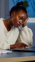 Exhausted african freelancer resting head on hand in front of laptop working overtime in start up company office. Stressed employee using modern technology doing overtime for deadline of project photo