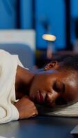 Dark skin freelancer doing overtime falling asleep with hand on desk trying to respect deadline for project. African employee working late at financial project sleeping on table in strat up office photo