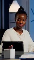 Multitasking black business woman working at laptop and tablet in same time doing overtime in start-up office. Busy african employee analysing financial statistics overworking writing, searching. photo