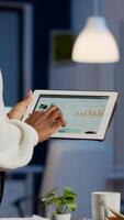 African freelancer woman holding tablet checking financial graphs standing in start-up office late at night. Businesswoman using social network, texting and blogging working overtime for job photo
