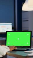 African manager typing at laptop with chroma key display during night time in start up business office working overtime. Freelancer watching mockup desktop monitor with green screen, writing datas photo