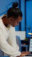 Stressed african manager woman working with financial documents checking graphs, holding papers, reading raports, standing at desk late at night in start-up office doing overtime to respect deadline. photo