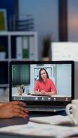 African businesswoman discussing with remotely woman partner online sitting in front of laptop working in start-up office talking on call during virtual meeting at midnight, using headphone photo