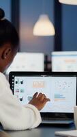 Black woman manager checking business statistics and financial reports on laptop working in start up office late at night. Focused employee doing overtime for job respecting deadline of project photo