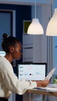 African businesswoman reading business reports from laptop in start up office late night typing new project. Focused employee doing overtime for job respecting deadline of project writing, searching photo