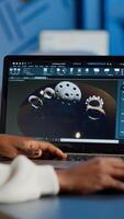 Tired african designer engineer analyzing new prototype of 3D model of industry product, working overtime. Industrial female worker studying gears idea on laptop showing cad software on device display photo