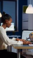 African engineer working late at night on a 3D model of industrial gears at laptop doing overtime in start up office. Freelancer studying prototype idea on pc showing cad software on device display photo