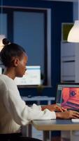 Dark skin gamer developer working at game in midnight from business office using professional laptop. African player testing online games on pc with modern technology network wireless. photo