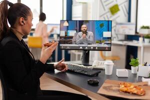 Businesswoman having delivery takeaway lunch meal order during takeout lunchtime at desk during online videocall meeting conference with remote manager. Entrepreneur eating pizza at workplace photo