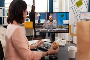 Entrepreneur woman sitting at desk in company office eating sandwich during online videocall conference meeting discussing financial strategy. Takeout order food delivery in corporate job place photo
