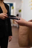 Entrepreneur using smartphone for money transaction with no card, for playing delivery guy bringing fresh tasty delicious meal lunch in paper bag. Client recieving takeaway food at workplace. photo