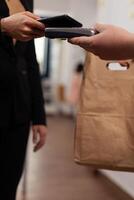 Customer paying for their order with smartphone nfc technology. Money transaction without credit card, recieving food order in paper bag. Using pos for takeaway pay. photo