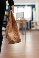 Businesswoman holding paper bag with takeaway food meal order putting on desk during takeout lunchtime in company office. Delivery man delivering fastfood packet for businesspeople. photo