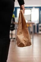 Businesswoman holding delivery takeaway food meal order paper bag during takeout lunchtime putting at desk in startup company office. Entrepreneur woman having lunch service while working at strategy photo