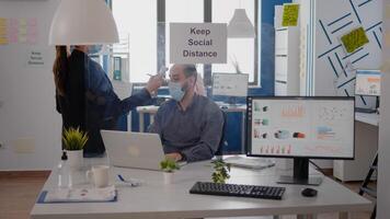 Adult woman with medical face mask measure team temperature using infrared thermometer. Coworkers respecting social distance in new normal company office to avoid infection with virus disease photo