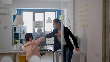 Coworkers touching elbow to avoid infection with coronavirus, business team wearing medical face mask while sitting on table desk working on company project respecting social distance photo