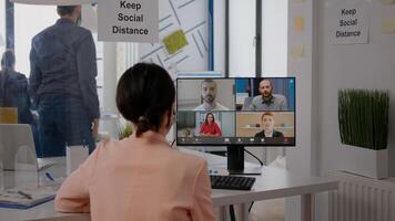 Business woman with face mask talking with team about communication project during online videocall meeting. Executive freelancer sitting at desk table in new normal office photo