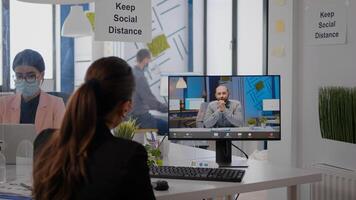 Back view of business woman with face mask disscusing on videocall conference with remotely coworkers. Executive freelancer working in new normal company office during coronavirus pandemic photo