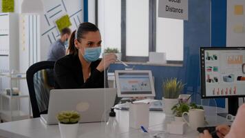 Close up of coworkers with face mask working together at financial project using tablet computer while sitting in company office. Team mantain social distance to avoid infection with covid19 photo