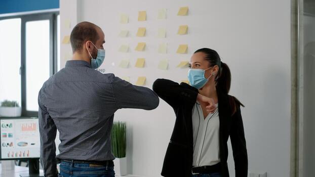 Coworkers with face mask touching elbow with his collegue to prevent infection with coronavirus. Coworkers respecting social distancing while working on communication company project photo